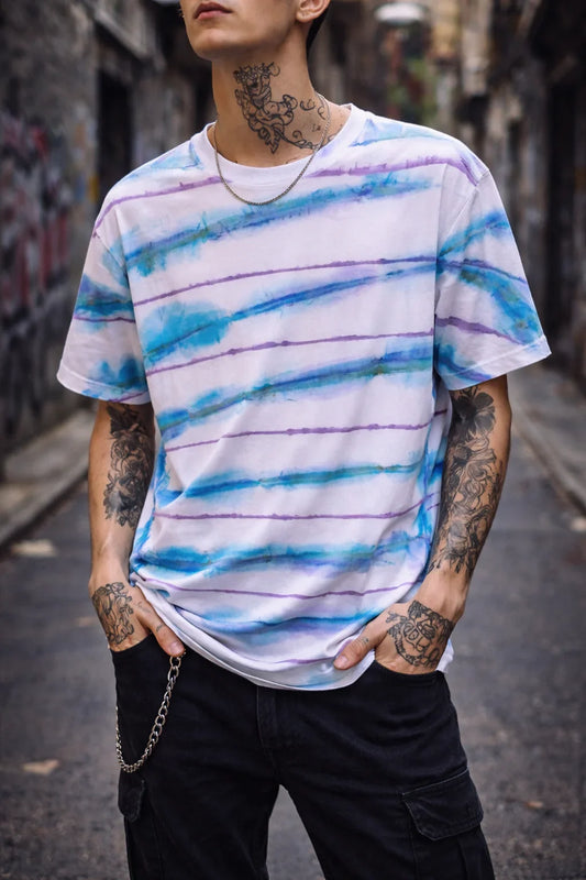 Camiseta blanca pintada a mano con rayas azul y morado, look urbano y tatuajes visibles.